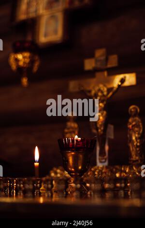 Candles on stand with candlesticks burning on altar in front of crucifixion of Jesus, holy virgin Mary and apostle John. Stock Photo