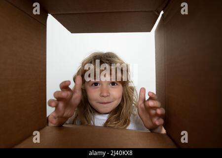 Surprised child boy unpacking, opening carton box and looking inside. Open box and delivery parcel for children. Children emotions and kids facial Stock Photo