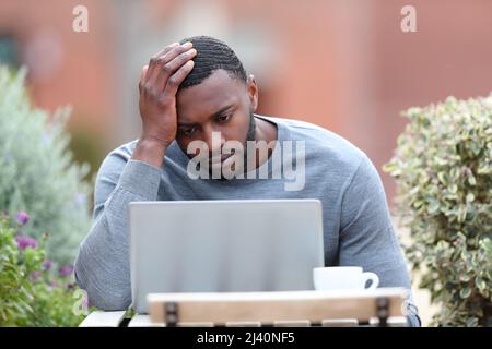 Front view portrait of a concerned man with black skin using laptop in a bar terrace Stock Photo