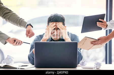 Maybe if I ignore them, theyll go away. Shot of a handsome young businessman sitting in the office and feeling stressed while his colleagues put Stock Photo