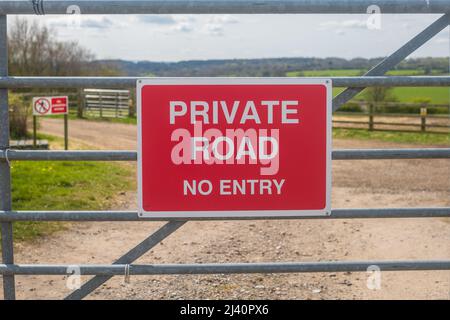 Private Road No Entry sign on a metal gate to a farm. Red and white signage. Stock Photo