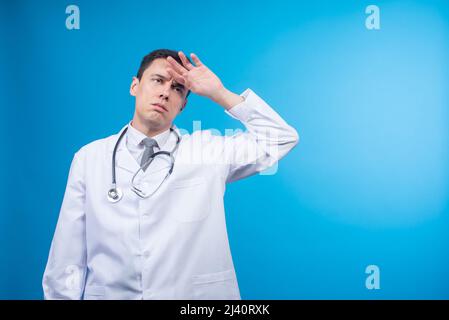 Exhausted male doctor touching forehead in studio Stock Photo