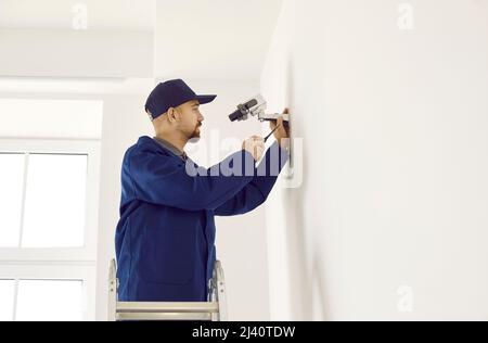 Male technician installing digital CCTV surveillance camera on wall inside building Stock Photo