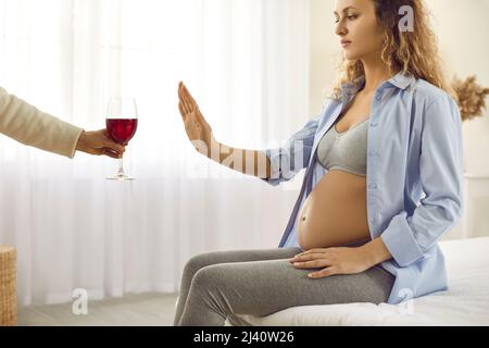 Pregnant woman being offered glass of wine doing stop gesture and refusing to drink Stock Photo