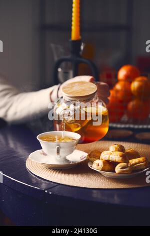 Water pours from a blue teapot into a glass mug containing dried purple ...