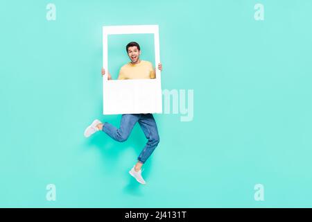 Full length portrait of overjoyed childish man hold paper card window isolated on turquoise color background Stock Photo