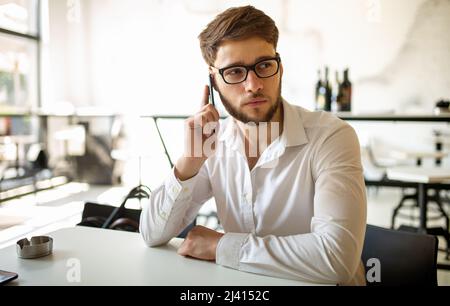 Portrait of a young business man using smart phone and working in cafe. Stock Photo