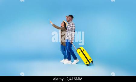 Cheery millennial black couple walking with suitcase, traveling together, having summer vacation on blue studio background Stock Photo