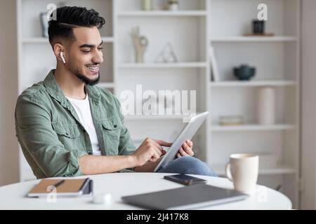 Modern Technologies. Smiling Young Arab Guy Using Digital Tablet At Home Stock Photo