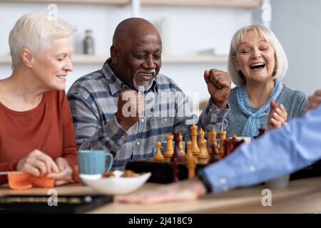 Emotional black man playing chess with multiracial friends Stock Photo