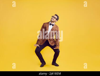 Happy funny goofy black man in leopard jacket dancing on yellow studio background Stock Photo