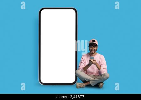 Cheerful hindu guy hipster sitting by huge smartphone Stock Photo