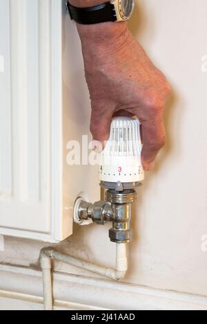 Turning down the heating to save money. Using a thermostatic radiator valve fitted to a room radiator. Stock Photo