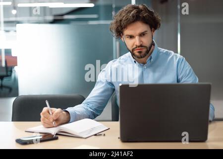 Portrait of focused man using laptop and writing Stock Photo