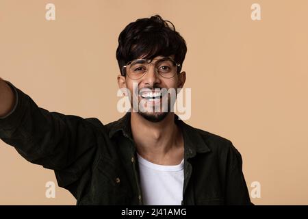 Positive indian man taking selfie on beige studio background Stock Photo