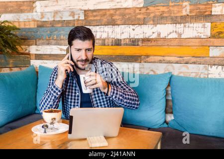 Freelancer talking on phone while looking at screen tablet in coffee shop Stock Photo
