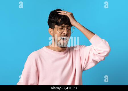 Overwhelmed indian guy touching his head, blue studio background Stock Photo