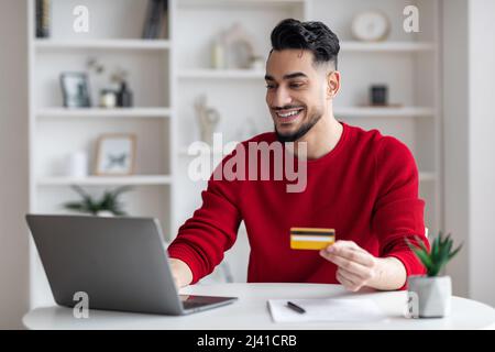 Online Payments Concept. Handsome Arab Guy Using Laptop And Credit Card Stock Photo