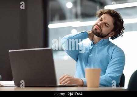 Tired man sitting at desk using pc, massaging neck Stock Photo