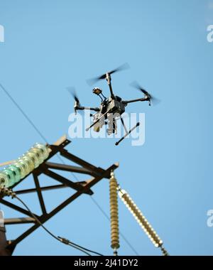Pro quadcopter with camera aboard flying in a sky, electric pylon, cables and insulators Stock Photo