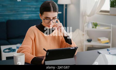 University student taking notes on digital tablet with stylus, using gadget to learn educational course for online school class. Woman working on device to prepare for remote homework lesson. Stock Photo