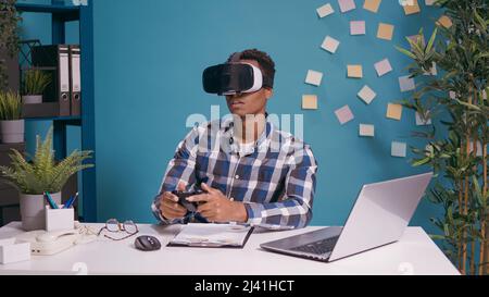 Modern man playing video games on vr goggles and console, using virtual reality headset and controller for fun. Person enjoying 3d visual simulation glasses with joystick at desk. Stock Photo