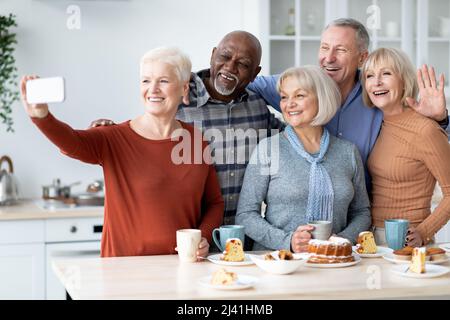 Positive multiethnic senior friends taking selfie at kitchen Stock Photo