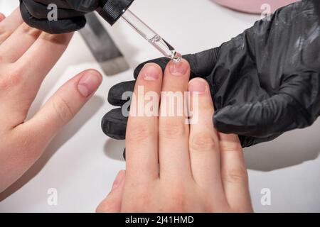 Applying oil on the nail to nourish and treat the cuticle after manicure, close-up. Hands during a manicure care session in a spa salon. Manicurist fi Stock Photo