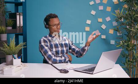Sales agent using headphones to answer customer service call, giving support and assistance to people calling on helpline. Operator working at call center, talking to client for telemarketing. Stock Photo