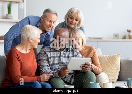 Cheerful elderly people spending time together at home, using gadgets Stock Photo