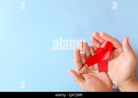 Top view of male hand holding red ribbon on blue background. AIDS, HIV, heart disease and stroke awareness concept. Stock Photo