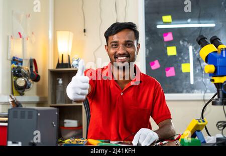 Happy repairman showing thumbs up sign by looking at camera while at mobile repair shop - concept of recommendation, approval and successful small Stock Photo