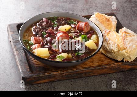 Stone soup of red beans, potatoes, chorizo, black pudding close-up in a bowl on a wooden tray. horizontal Stock Photo