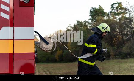 Firefighter at action taking hose from fire truck outdoors in nature. Stock Photo