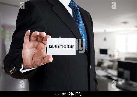 Businessman shows a business card with the word questions. Business assistance, customer support concept. Stock Photo
