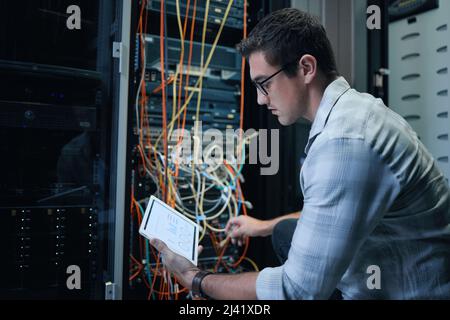 Running diagnostics. Cropped shot of a handsome young male programmer working on a tablet in a server room. Stock Photo