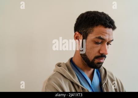 Depressed young male doctor or caregiver over beige background. Stock Photo