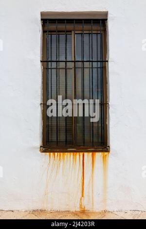 Window with old grate dripping rust on the white wall Stock Photo