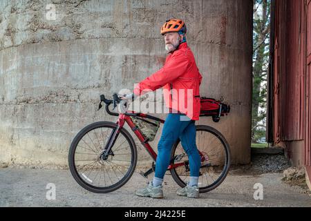senior male cyclist with a gravel bike taking a break at old barn in Colorado coutryside Stock Photo