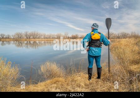 senior male paddler wearing life jacket with a wooden canoe paddle on a ...