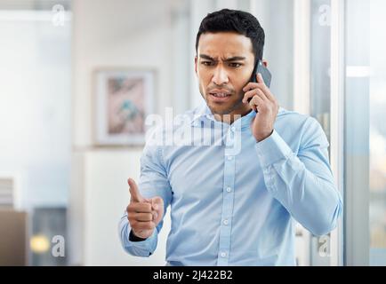 You have a deadline and need to stick to it. Shot of a young businessman looking angry while making a phone call using his smartphone. Stock Photo