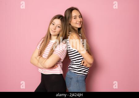 Portrait of two cheerful young women standing together and looking at camera isolated over pink background Stock Photo