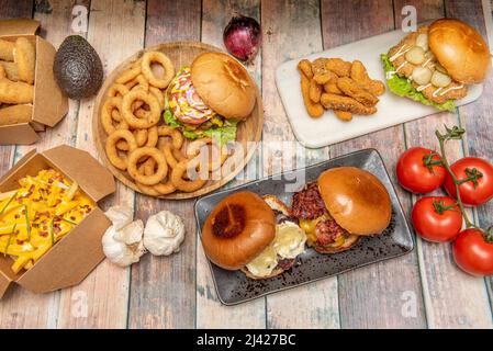 Set of fast homemade food dishes with assorted burgers, nachos with guacamole and nacho cheese, homemade fries, fried onion rings, chicken fingers and Stock Photo
