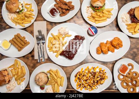 American fast food dishes set with assorted burgers, home fries, fried onion rings, buffalo wings, chicken wings, mozzarella fingers, bbq ribs and fre Stock Photo