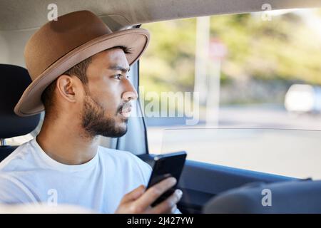 Its not the destination, its the journey. Shot of a young man sitting in a car while using his phone. Stock Photo