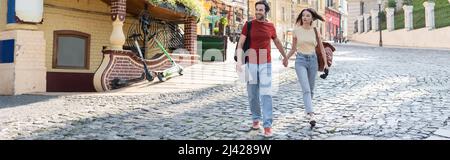 Couple of travelers with map and binoculars holding hands while walking on urban street, banner Stock Photo