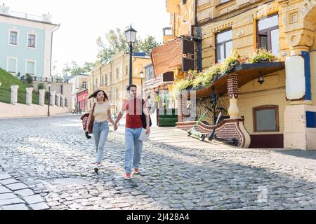 Happy tourist holding map and hand of girlfriend while walking on urban street Stock Photo