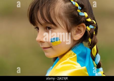 Close-up portrait of a small beautiful Ukrainian girl with two pigtails with yellow and blue ribbons like the Ukrainian flag. She asks for help to save Ukraine. Stop the war. High quality photo Stock Photo