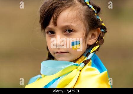 Close-up portrait of a small beautiful Ukrainian girl with two pigtails with yellow and blue ribbons like the Ukrainian flag. She asks for help to save Ukraine. Stop the war. High quality photo Stock Photo