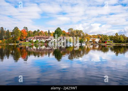Modern lakeside brick row houses surrounded by colourf trees at the peak of fall foliage on a partly cloudy morning. Reflection in water. Stock Photo